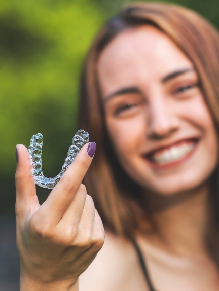 Smiling teenage girl holding an Invisalign clear aligner in Fort Lauderdale
