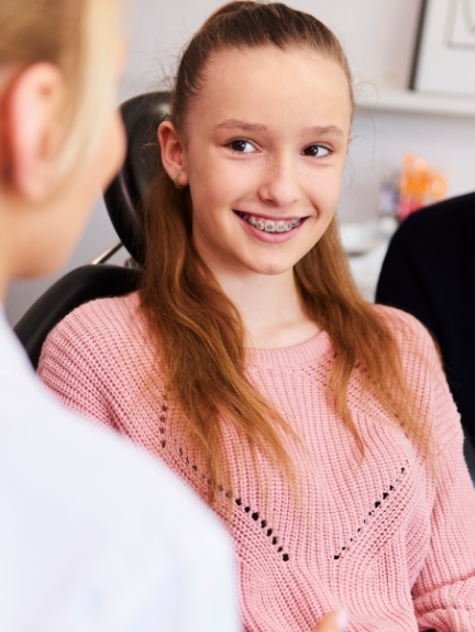 Teen girl in dental chair smiling with traditional braces