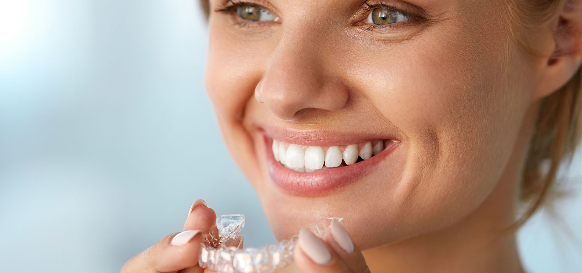 Young woman smiling with Invisalign Aligners in her hand.