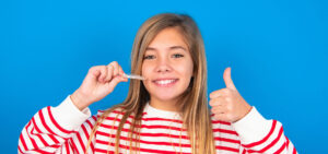 High School girl smiling with with thumbs up holding her Invisalign aligners.