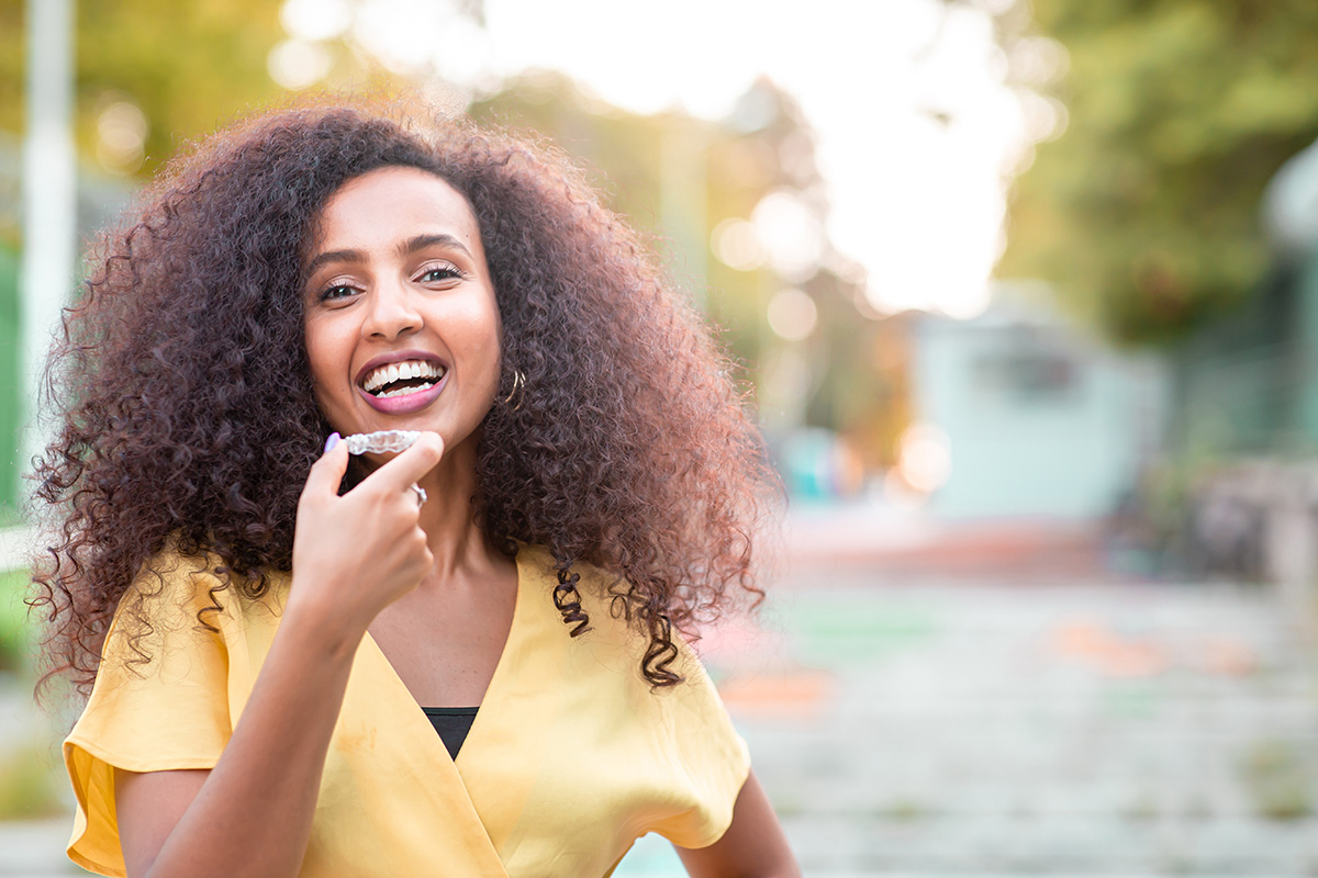 Beautiful smiling woman holding invisalign aligner.