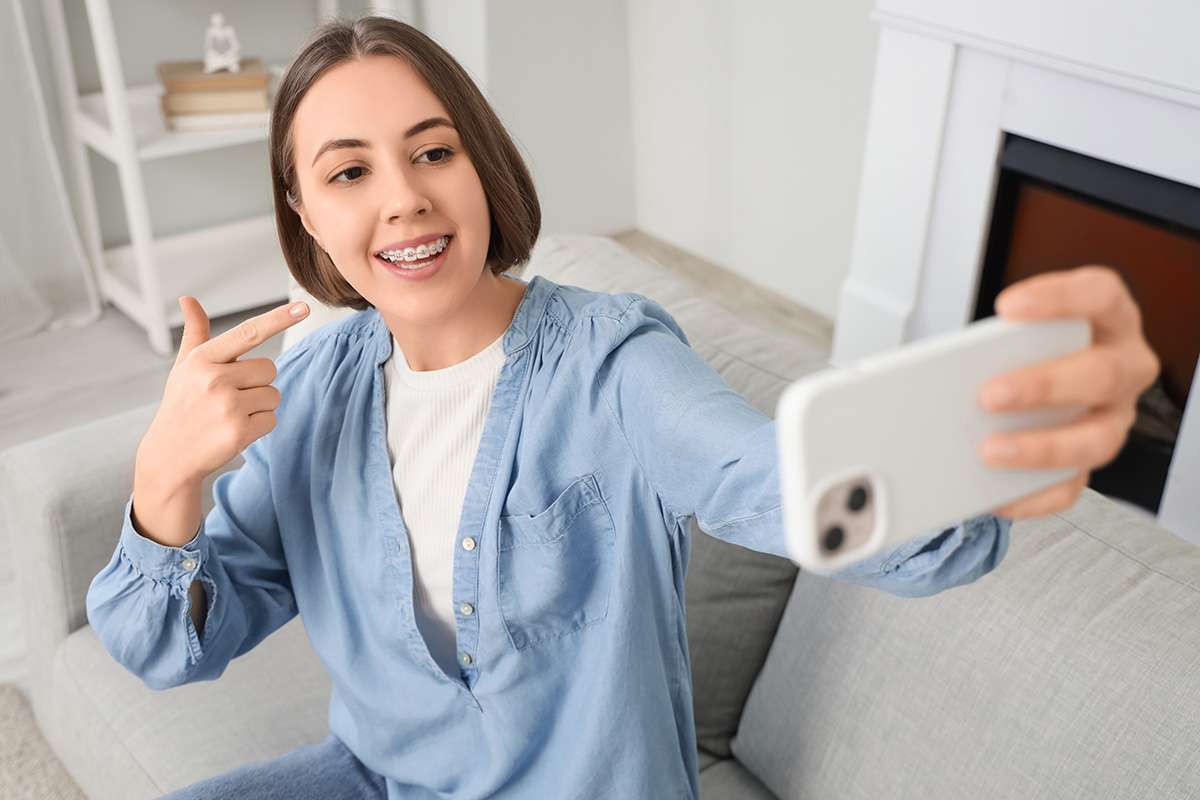 Young woman with dental braces taking selfie at home