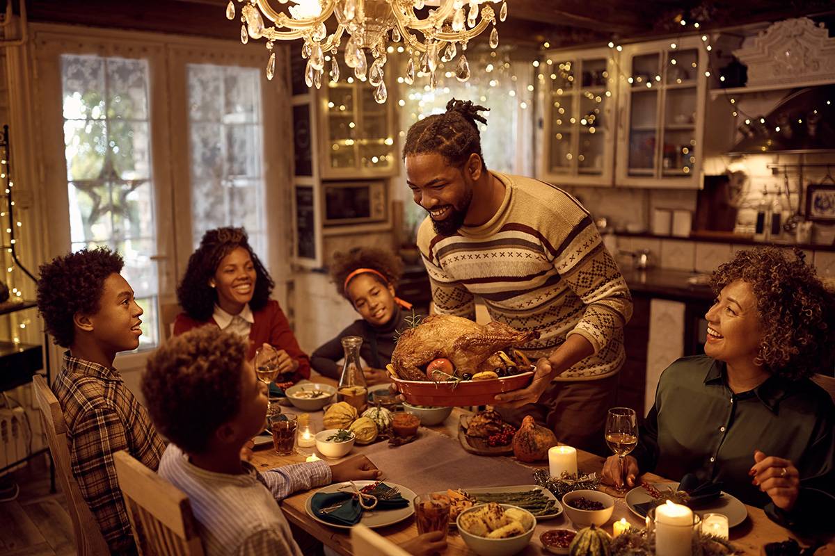 Man serving stuffed turkey while having dinner with his family on Thanksgiving.