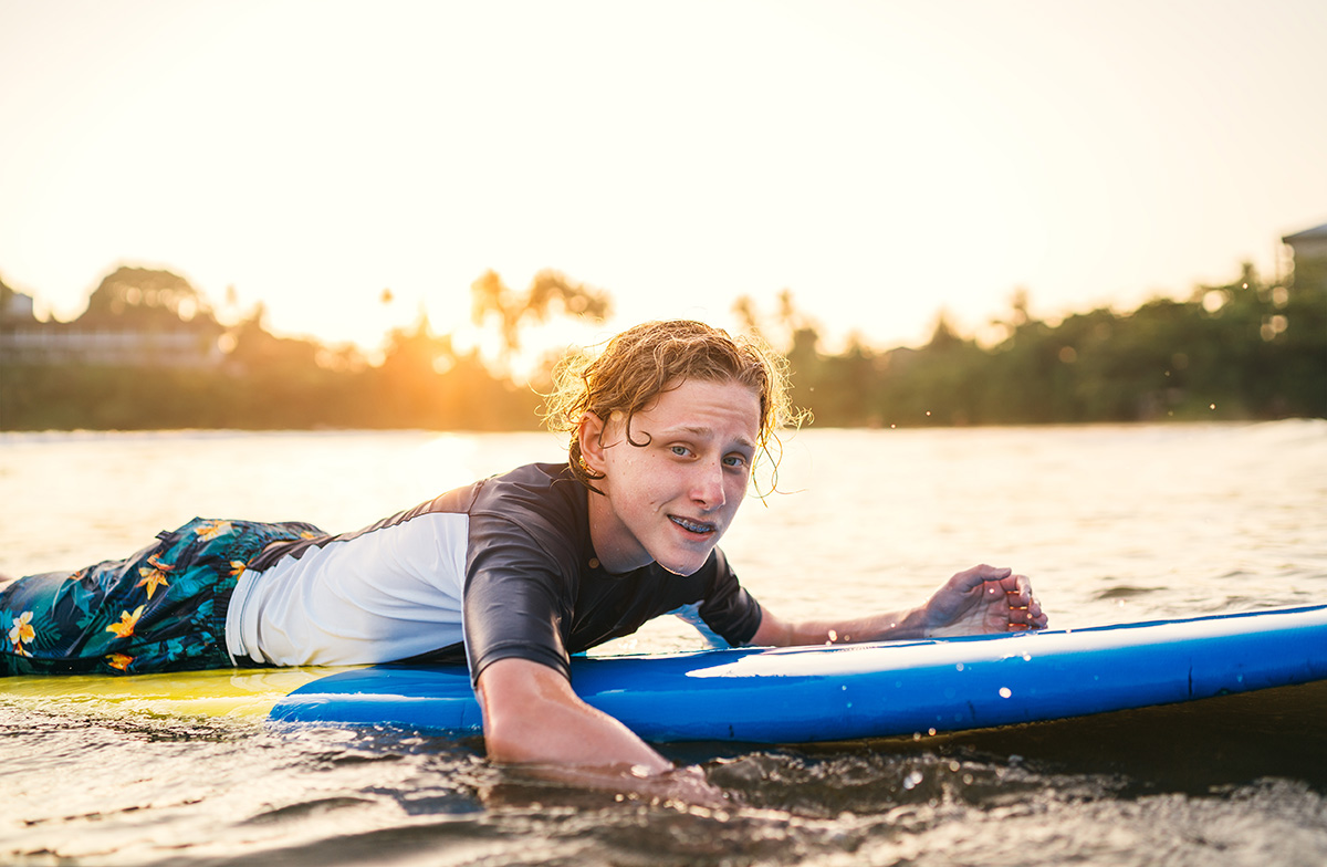 Boy with dental braces floating on surfboard.