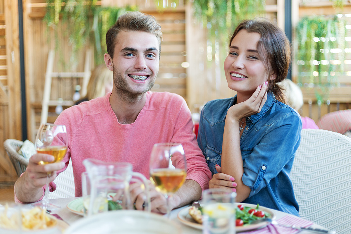 Happy young couple smiling while having dinner in restaurant, handsome man wearing dental braces