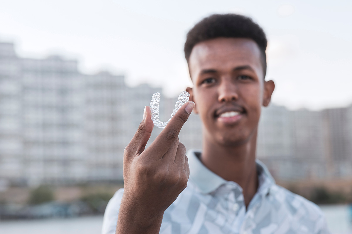 Young man is holding an Invisalign brace and he has confident smiling