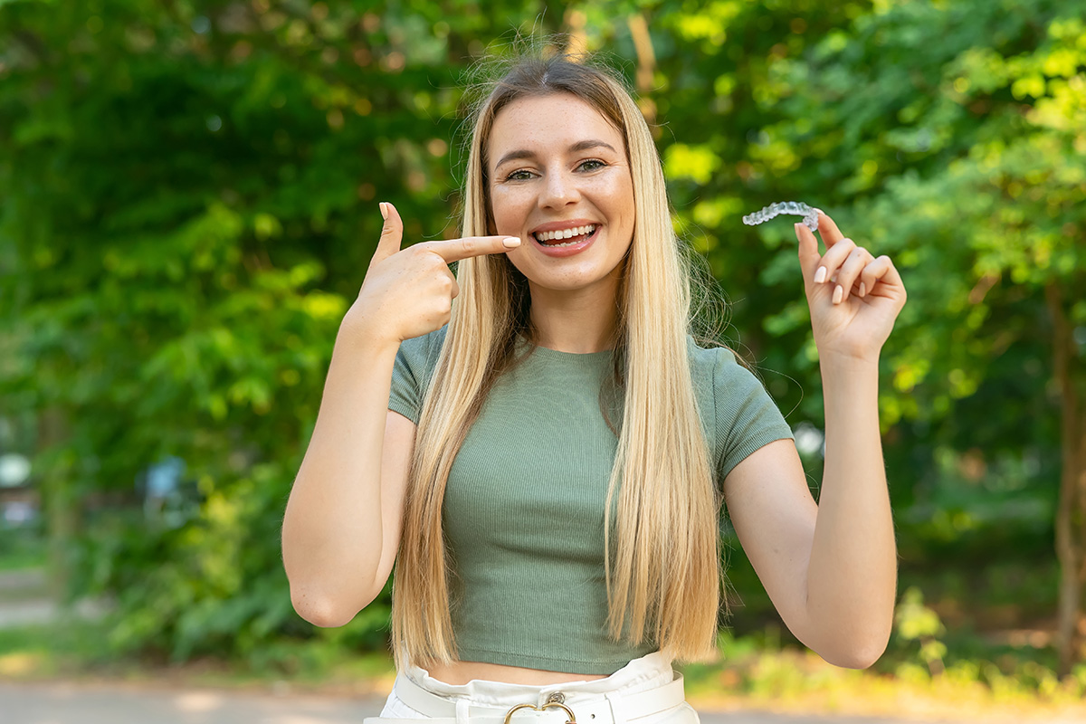 Young beautiful woman holding an invisible aligner and pointing at it. 