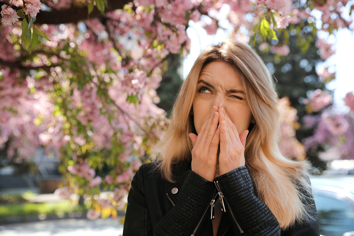 Woman suffering from seasonal pollen allergy near blossoming tree 