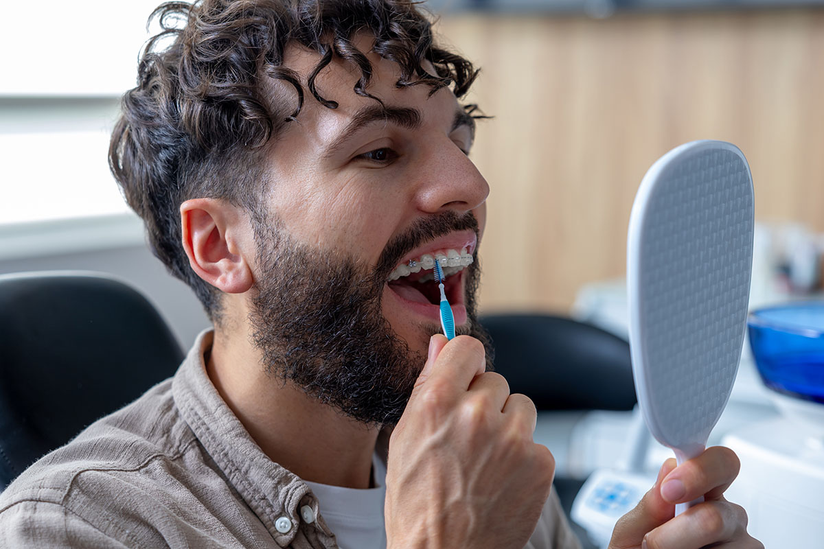 Man with metal braces carefully cleaning his teeth using interdental brush focusing on removing debris between brackets to maintain proper dental hygiene