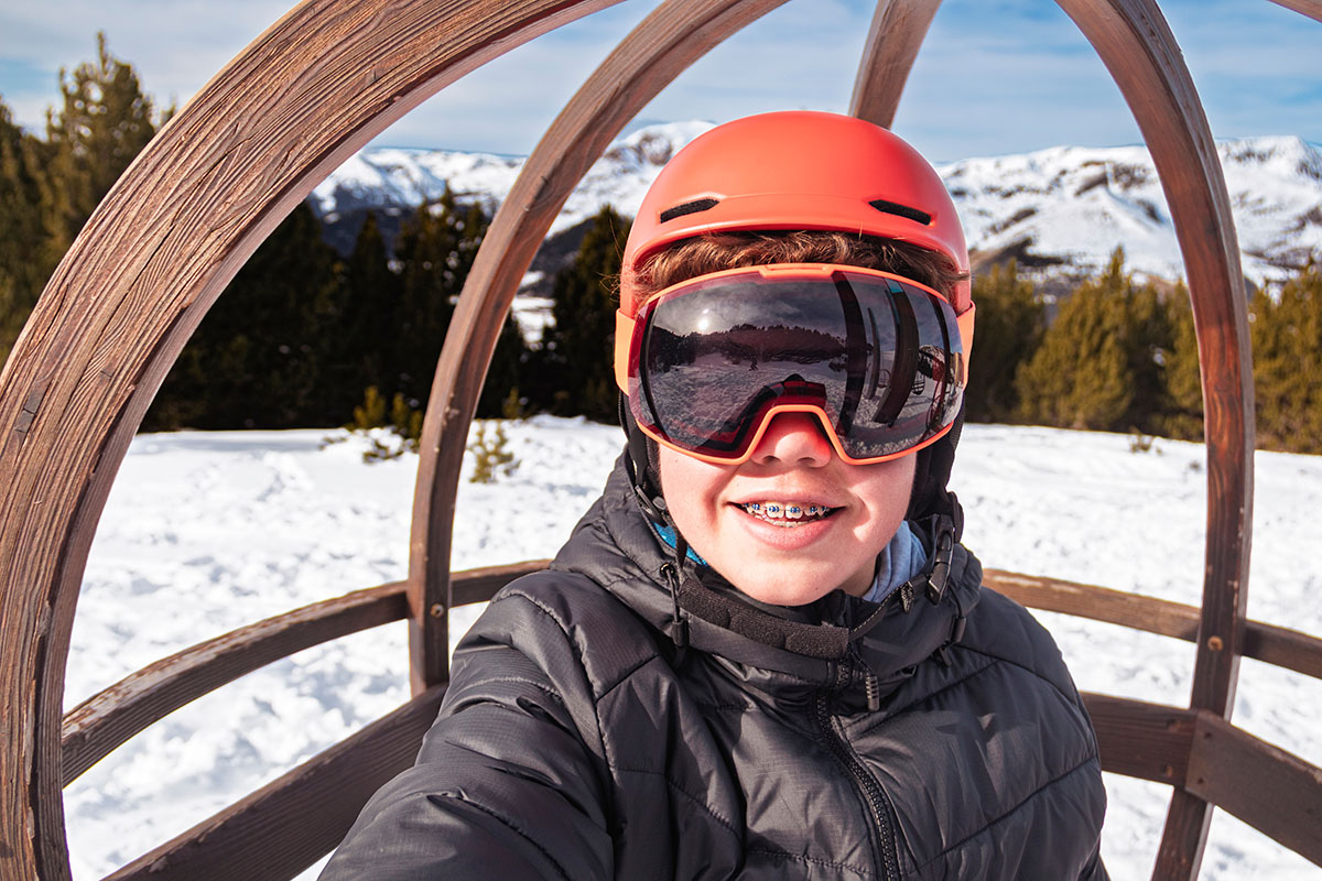 Young boy smiling, wearing ski gear and braces, enjoying winter vacation in snowy mountains