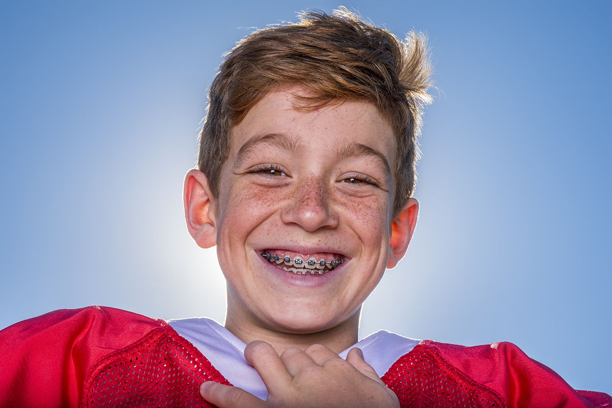Freckled young football player with braces smiling outside
